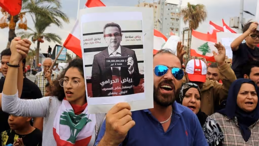 Demonstrators carry Lebanese flags and a banner depicting Lebanon's central bank governor, Riad Salameh, as they head towards the central bank building during an anti-government protest in the southern city of Tyre, Lebanon. Photo: Aziz Taher/Reuters.