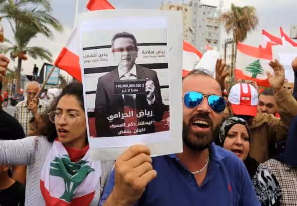 Demonstrators carry Lebanese flags and a banner depicting Lebanon's central bank governor, Riad Salameh, as they head towards the central bank building during an anti-government protest in the southern city of Tyre, Lebanon. Photo: Aziz Taher/Reuters.
