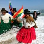 Bolivian women traditionally dressed and hanging Wiphala and Bolivian flags take a splash in a beach. Photo: File photo.