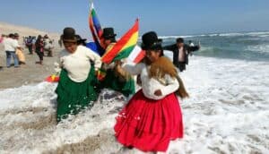 Bolivian women traditionally dressed and hanging Wiphala and Bolivian flags take a splash in a beach. Photo: File photo.