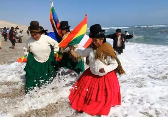 Bolivian women traditionally dressed and hanging Wiphala and Bolivian flags take a splash in a beach. Photo: File photo.