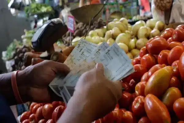 Person counting Venezuelan bank notes in a popular market vegetable stand with tomatoes and onions in the background. Photo: Misión Verdad/file photo.