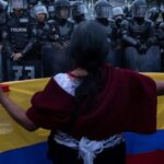 Woman holding an Ecuadorian flag in front of police barrier. Photo: Eduardo de Leon Herencia,