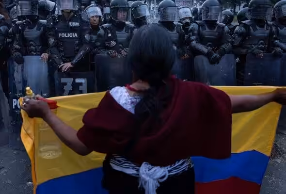 Woman holding an Ecuadorian flag in front of police barrier. Photo: Eduardo de Leon Herencia,