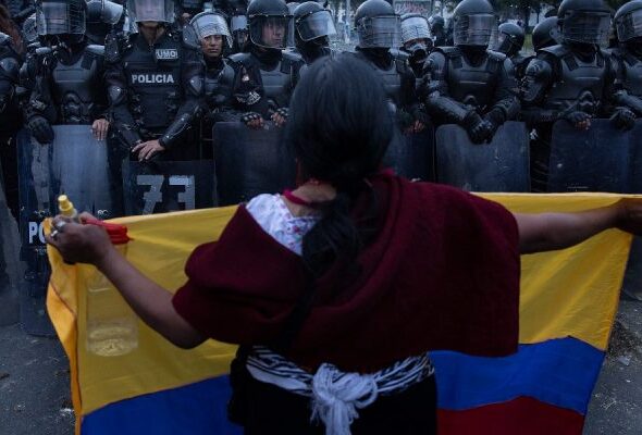 Woman holding an Ecuadorian flag in front of police barrier. Photo: Eduardo de Leon Herencia,