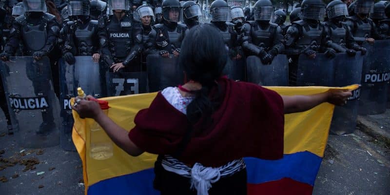 Woman holding an Ecuadorian flag in front of police barrier. Photo: Eduardo de Leon Herencia,