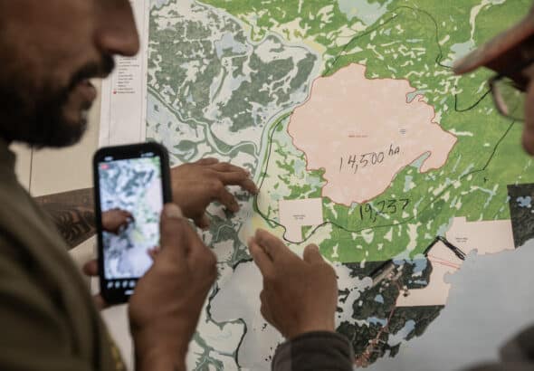 People look at a map of the fire in Fort Chipewyan, Alberta on Friday, June 2, 2023. Over 800 people have been evacuated from Fort Chipewyan as wildfires threaten the community downriver from the oil sands. Photo: Amber Bracken.