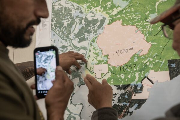 People look at a map of the fire in Fort Chipewyan, Alberta on Friday, June 2, 2023. Over 800 people have been evacuated from Fort Chipewyan as wildfires threaten the community downriver from the oil sands. Photo: Amber Bracken.