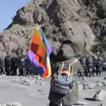 Protester holding a Wiphala flag faces a large group of riot police in Jujuy, Argentina. Photo: Susi Maresca.