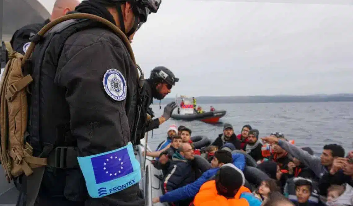 A FRONTEX official stands before a boat carrying migrants. Photo: MasarBadil.org.