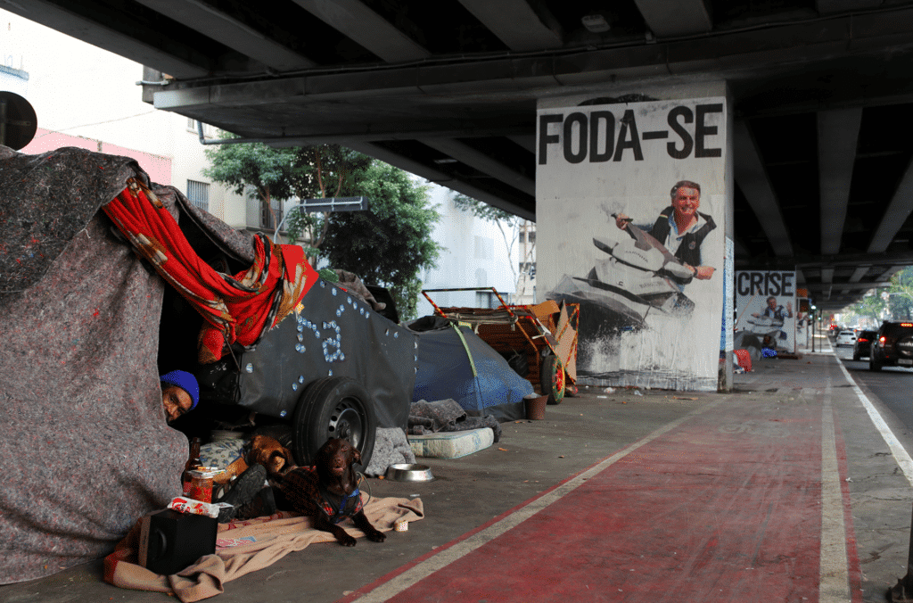 A poster depicting Jair Bolsonaro driving a jet ski below the words "fuck you" near a homeless encampment in São Paulo, Brazil. Photo: Amanda Perobelli/Reuters.