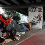 A poster depicting Jair Bolsonaro driving a jet ski below the words "fuck you" near a homeless encampment in São Paulo, Brazil. Photo: Amanda Perobelli/Reuters.