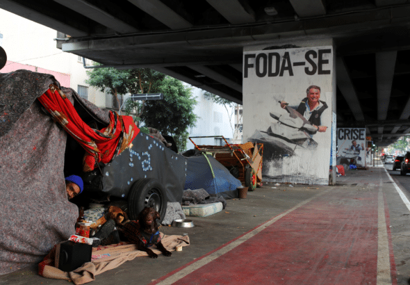 A poster depicting Jair Bolsonaro driving a jet ski below the words "fuck you" near a homeless encampment in São Paulo, Brazil. Photo: Amanda Perobelli/Reuters.
