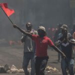 A man waves a red flag during a protest against fuel price hikes. Photo: AP/Odelyn Joseph.