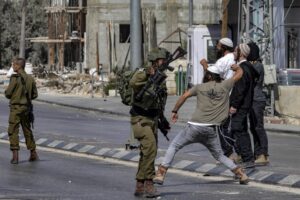 Soldiers of the apartheid state stand by as Zionist settlers throw stones at Palestinians during clashes in the town of Huwara in the West Bank on October 13, 2022. Photo: Oren Ziv/AFP.