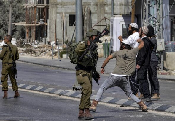 Soldiers of the apartheid state stand by as Zionist settlers throw stones at Palestinians during clashes in the town of Huwara in the West Bank on October 13, 2022. Photo: Oren Ziv/AFP.