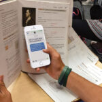Student in class texting on a cellphone that is hidden by a larger book. Photo: Scholastic/file photo.