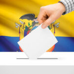 A hand inserts a ballot into a ballot box, with the flag of Ecuador in the background. File photo.