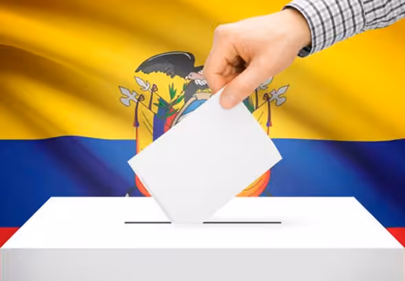 A hand inserts a ballot into a ballot box, with the flag of Ecuador in the background. File photo.