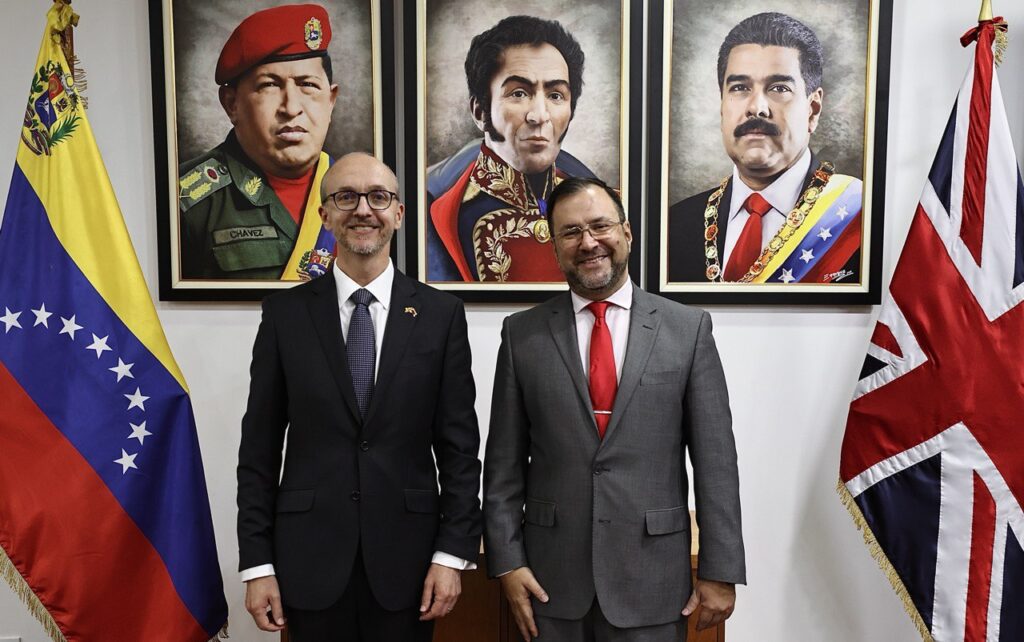 New UK head of diplomatic mission in Venezuela Colin Dick (left) next to Venezuelan Foreign Minister Yvan Gil (right), with portraits of Hugo Chávez, Simón Bolívar, and President Nicolás Maduro in the background, framed by the flags of both countries. Photo: X/yvangil.