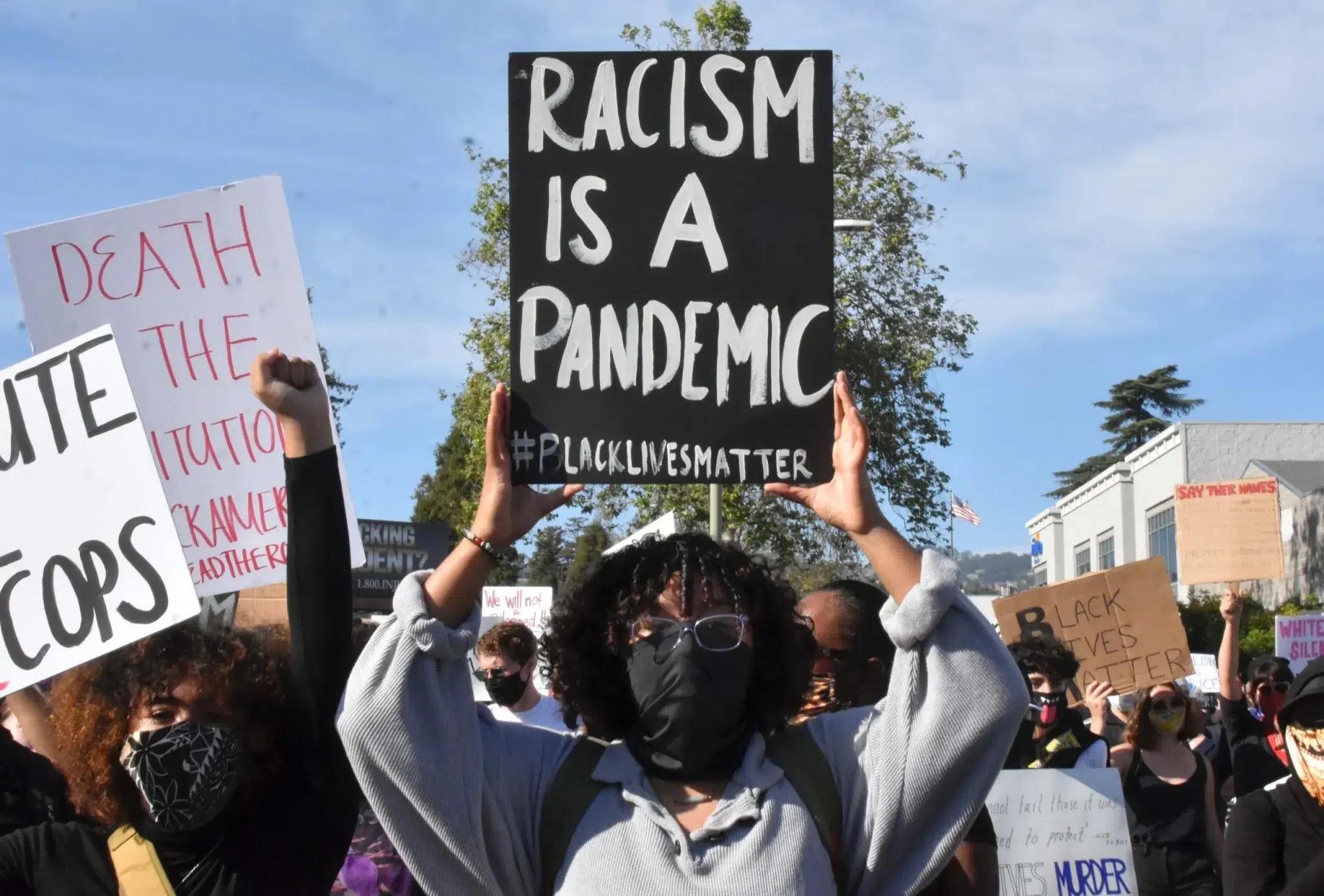 A woman at a rally holds up a sign that reads: Racism is a Pandemic. Photo: Bill Hackwell.