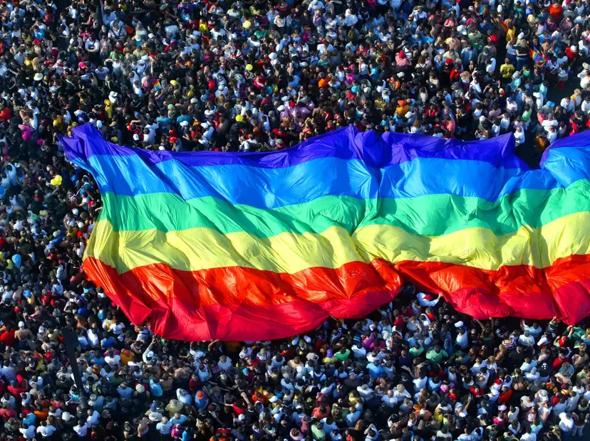 An LGBTQIA+ Pride flag is carried by a marching crowd of supporters. Photo: Getty Images.