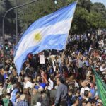 Argentinian demonstrators hold up a flag of Argentina amidst a large crowd of fellow demonstrators. Photo: Prensa Latina.