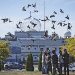 A flock of birds flies past as Moninder Singh, front right, a spokesperson for the British Columbia Gurdwaras Council (BCGC), as he waits to speak to reporters outside the Guru Nanak Sikh Gurdwara Sahib in Surrey, British Columbia, on Monday, Sept. 18, 2023. Photo: Darryl Dyck/The Canadian Press via AP.