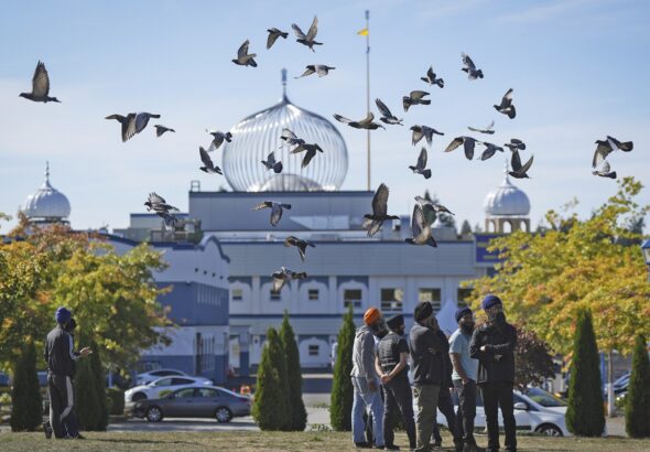 A flock of birds flies past as Moninder Singh, front right, a spokesperson for the British Columbia Gurdwaras Council (BCGC), as he waits to speak to reporters outside the Guru Nanak Sikh Gurdwara Sahib in Surrey, British Columbia, on Monday, Sept. 18, 2023. Photo: Darryl Dyck/The Canadian Press via AP.