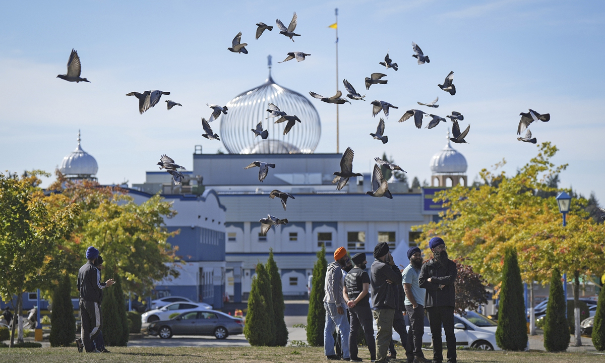 A flock of birds flies past as Moninder Singh, front right, a spokesperson for the British Columbia Gurdwaras Council (BCGC), as he waits to speak to reporters outside the Guru Nanak Sikh Gurdwara Sahib in Surrey, British Columbia, on Monday, Sept. 18, 2023. Photo: Darryl Dyck/The Canadian Press via AP.