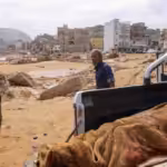 People walk past the body of a flash flood victim in Derna, eastern Libya, on September 11, 2023. Photo: AFP.