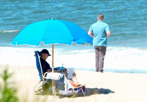 US President Joe Biden (left) and First Lady Jill Biden sit under an umbrella with a secret service agent nearby, in Rehoboth Beach, Delaware, on August 1, 2023. Photo: AFP.