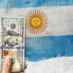Three American 100 dollar bills with a blurred Argentinian flag in the background. Photo: El Cronista/File photo.
