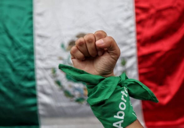 A fist raised high in resistance with a fabric wrapped around the wrist, captioned "aborto" (abortion), in front of a Mexican flag. Photo: Expansion Politica/File photo.