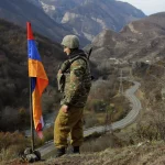 A soldier looks over a valley, standing next to the flag of Armenia. Photo: AP Photo/Sergei Grits.
