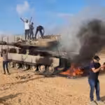 Palestinians celebrate next to a destroyed Israeli tank at the Gaza Strip fence on October 7, 2023. Photo: AP.