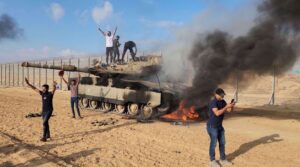 Palestinians celebrate next to a destroyed Israeli tank at the Gaza Strip fence on October 7, 2023. Photo: AP.