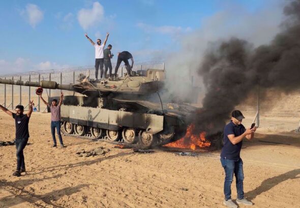 Palestinians celebrate next to a destroyed Israeli tank at the Gaza Strip fence on October 7, 2023. Photo: AP.