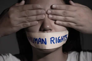 Young woman with her eyes covered with her hands and her mouth strapped with adhesive tape with a caption that reads Human Rights. Photo: Caitlin Johnstone/File Photo.