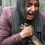 A wounded woman cries as she holds the hand of her dead relative outside her home following Israeli airstrikes in Gaza City, Oct. 23, 2023. Photo: Abed Khaled/AP.
