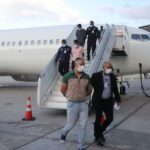 Three Venezuelans, recently repatriated from the United States, exiting the plane that brought them to Venezuela, handcuffed and escorted by law enforcement agents. Photo: X/@CeballosIchaso1.
