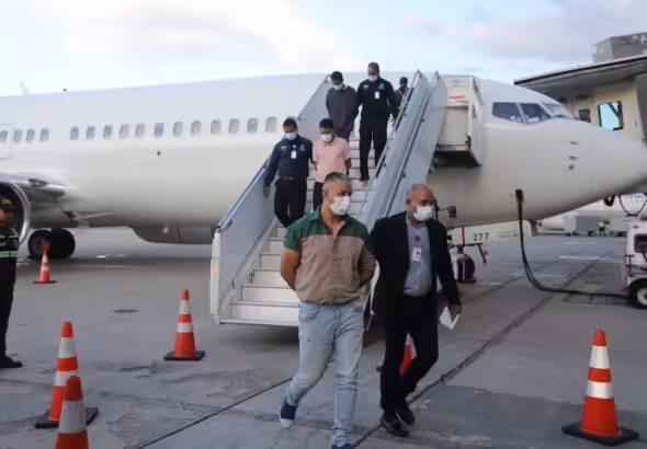 Three Venezuelans, recently repatriated from the United States, exiting the plane that brought them to Venezuela, handcuffed and escorted by law enforcement agents. Photo: X/@CeballosIchaso1.