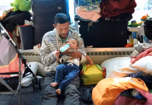 A migrant father from Venezuela feeds his 15-month-old son in the lobby of a police station where their family has been staying since their arrival to Chicago on May 9, 2023. Photo: Scott Olson/Getty