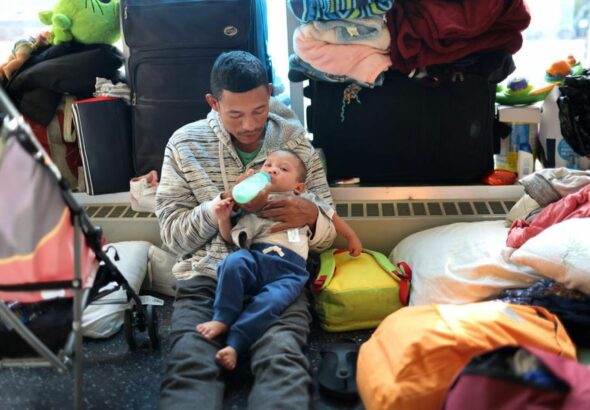 A migrant father from Venezuela feeds his 15-month-old son in the lobby of a police station where their family has been staying since their arrival to Chicago on May 9, 2023. Photo: Scott Olson/Getty