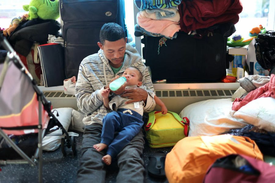 A migrant father from Venezuela feeds his 15-month-old son in the lobby of a police station where their family has been staying since their arrival to Chicago on May 9, 2023. Photo: Scott Olson/Getty