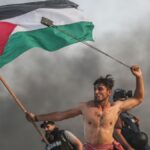 A man waves the Palestinian flag and throws rocks with a probe. Photo: Mustafa Hassouna.