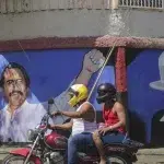 A motorcyclist rides past a mural of Nicaraguan President Daniel Ortega (left) and revolutionary hero César Augusto Sandino (right). Photo: Andres Nunes/AP.