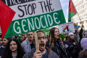 A demonstrator displays a placard with the lettering reading 'Stop the Genocide' during a rally in solidarity with the Palestinians in the Gaza Strip at Warsaw, Poland on October 29, 2023.  Photo by Wojtek Radwanski/AFP.