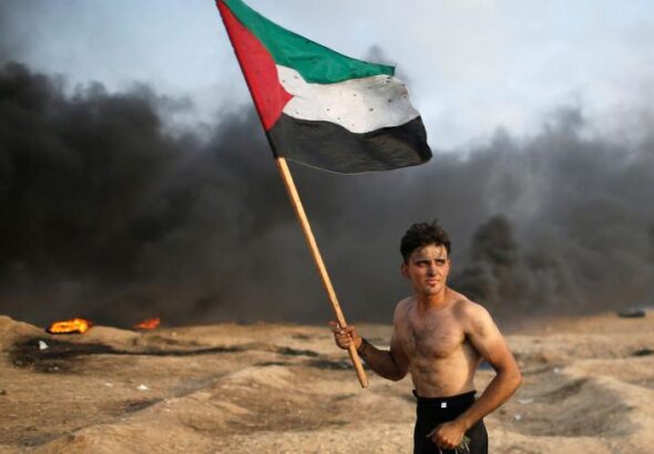 A Palestinian holds a Palestinian flag during a protest calling for lifting the Israeli blockade on Gaza and demanding the right to return to their homeland, at the Israel-Gaza border fence, Gaza Strip, Oct. 19, 2018. Photo: Reuters/Mohammed Salem.