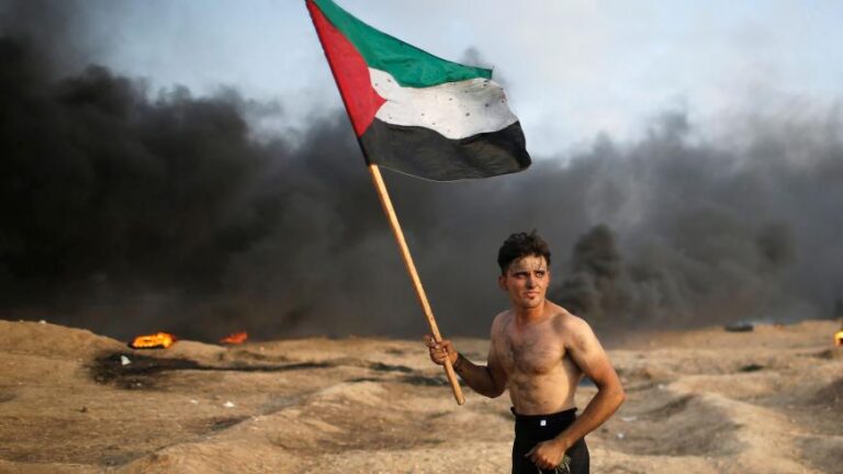 A Palestinian holds a Palestinian flag during a protest calling for lifting the Israeli blockade on Gaza and demanding the right to return to their homeland, at the Israel-Gaza border fence, Gaza Strip, Oct. 19, 2018. Photo: Reuters/Mohammed Salem.